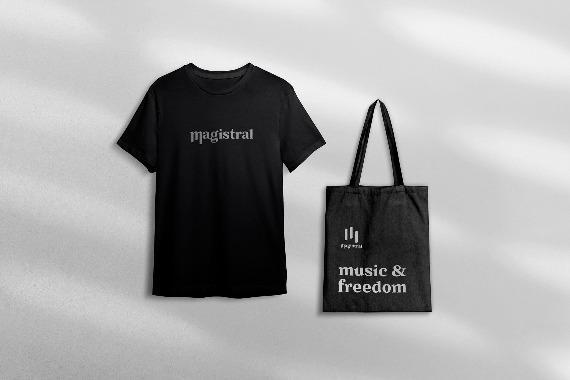 Mockup d’un t-shirt et d’un tote bag noirs mettant en scène l’identité visuelle “Magistral” conçue par Gaële Gerbaux du studio nueva vista pour un magasin d’instruments de musique : lettrage typographique sur le t-shirt et logo évoquant les touches de piano sur le tote bag, accompagné de la phrase “music & freedom”.