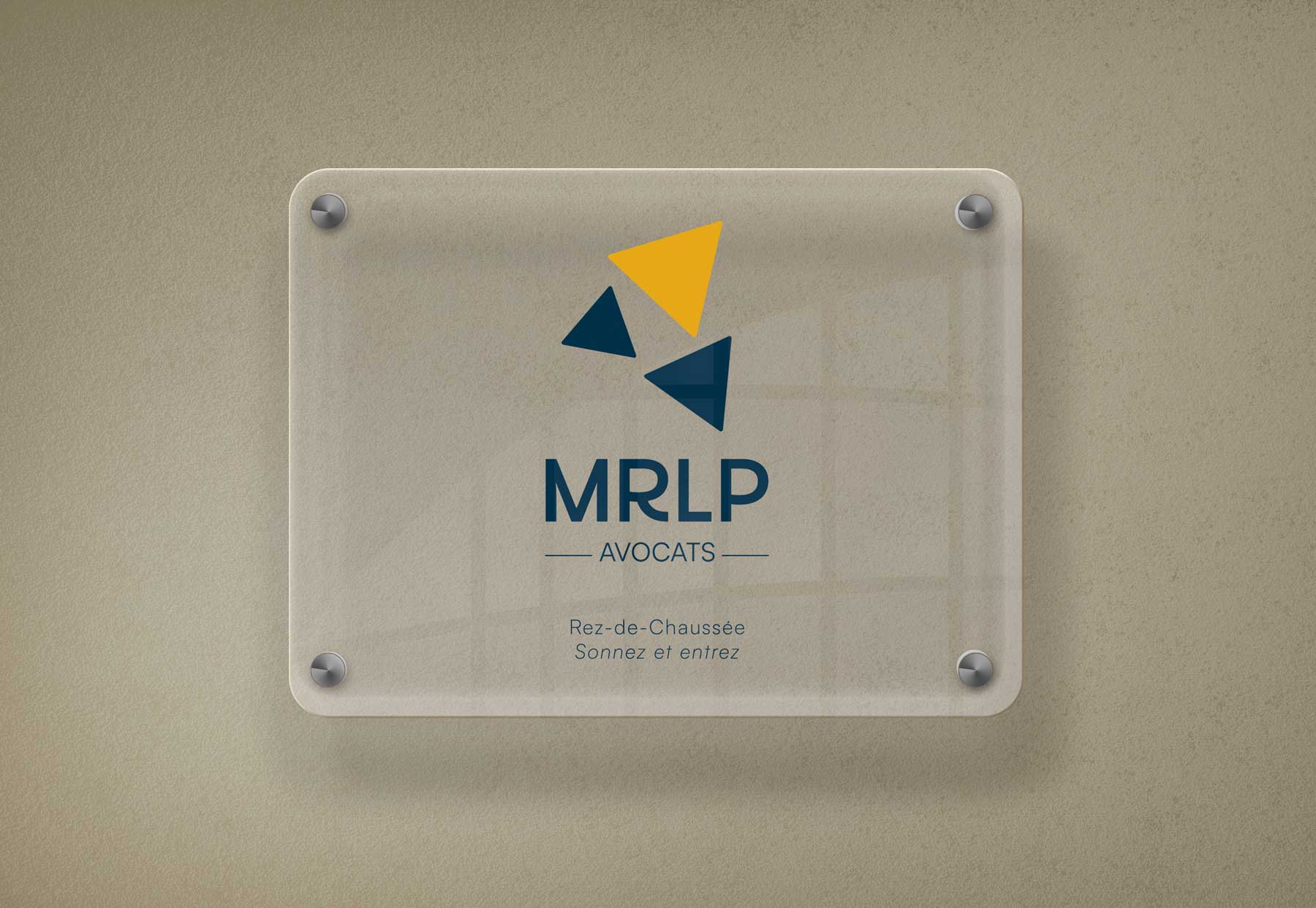 Plaque professionnelle en plexiglas fixée au mur, présentant le logo du cabinet “MRLP Avocats” conçu par Gaële Gerbaux du studio nueva vista : assemblage de triangles bleu marine et jaune formant un symbole géométrique moderne, accompagné du nom du cabinet et des indications « Rez-de-Chaussée – Sonnez et entrez ».