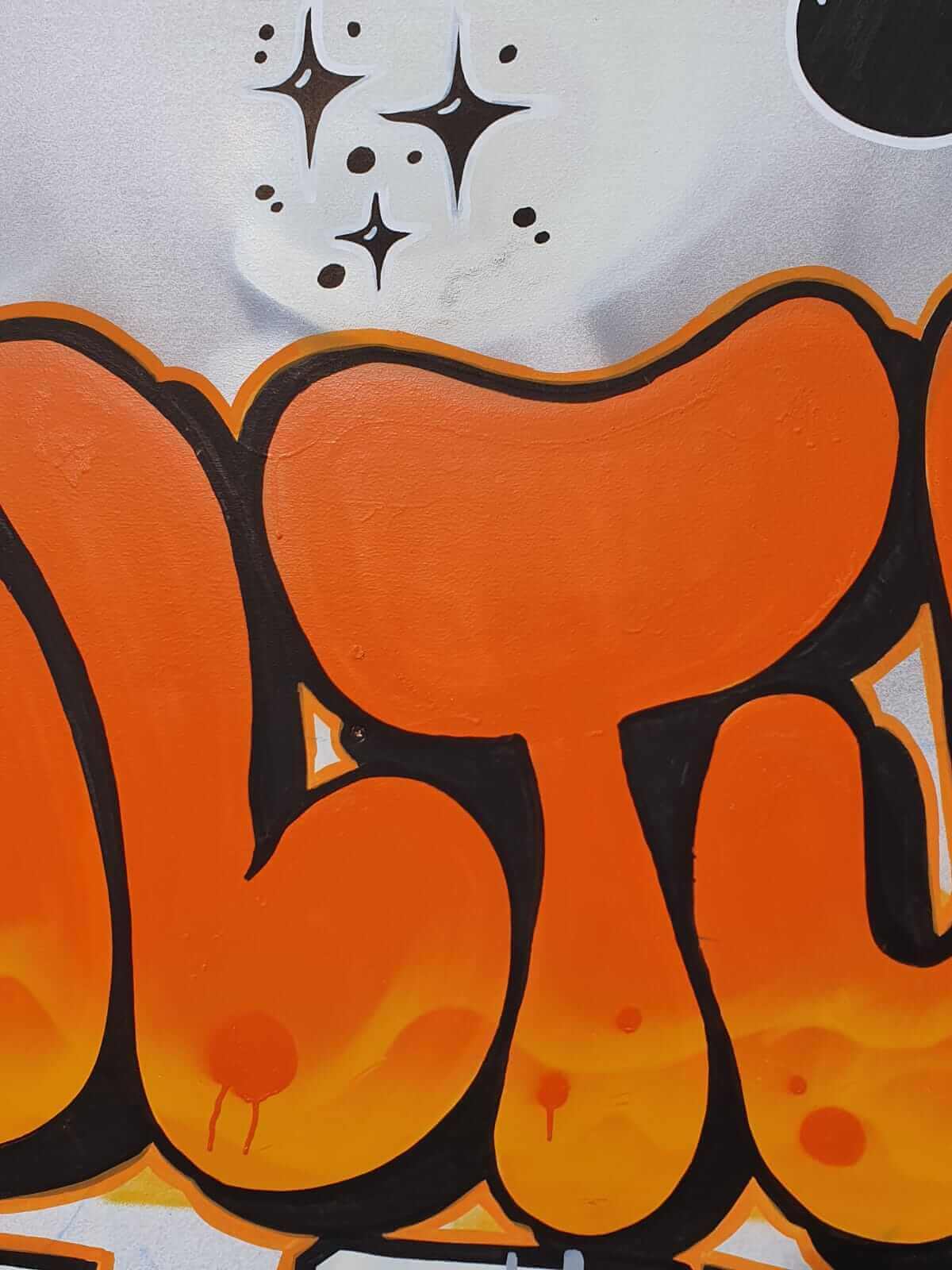 Gros plan sur le lettering orange de la fresque murale - bubble letters et motifs étoiles peints à la main, local jeunes Saint-Vigor le Grand