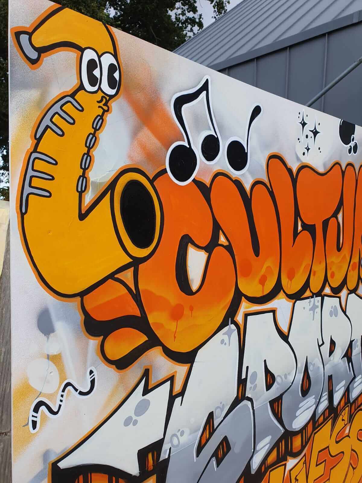 Personnage saxophone cartoon et lettering "Culture" en bubble letters oranges - détail de la fresque peinte à la main, CalvadosSonnet 4.6 Moyen